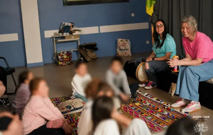Des enfants, visages floutés, assis en cercle sur un tapis berbère face aux deux conteuses.