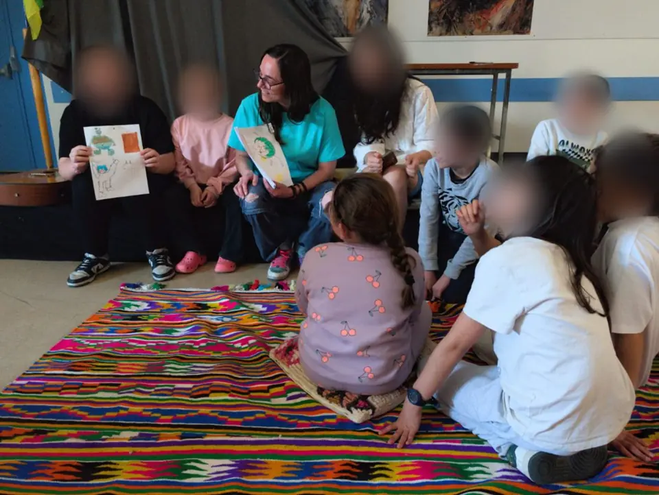 Des enfants aux visages floutés et une conteuse montrent les dessins réalisés pendant l'atelier.