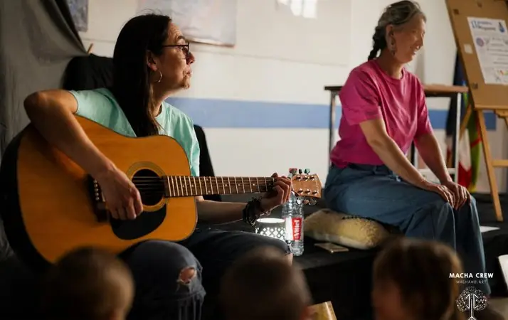 Les deux conteuses de la Macha Crew pendant un atelier : l'une joue de la guitare, l'autre l'écoute en souriant.